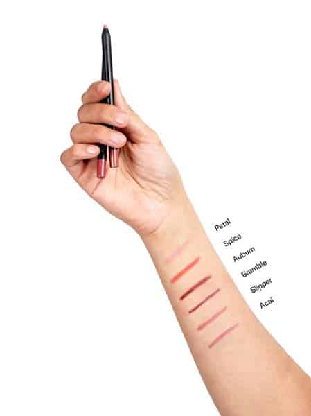 Hand holding two lip liners and six swatches on the back of the forearm. 